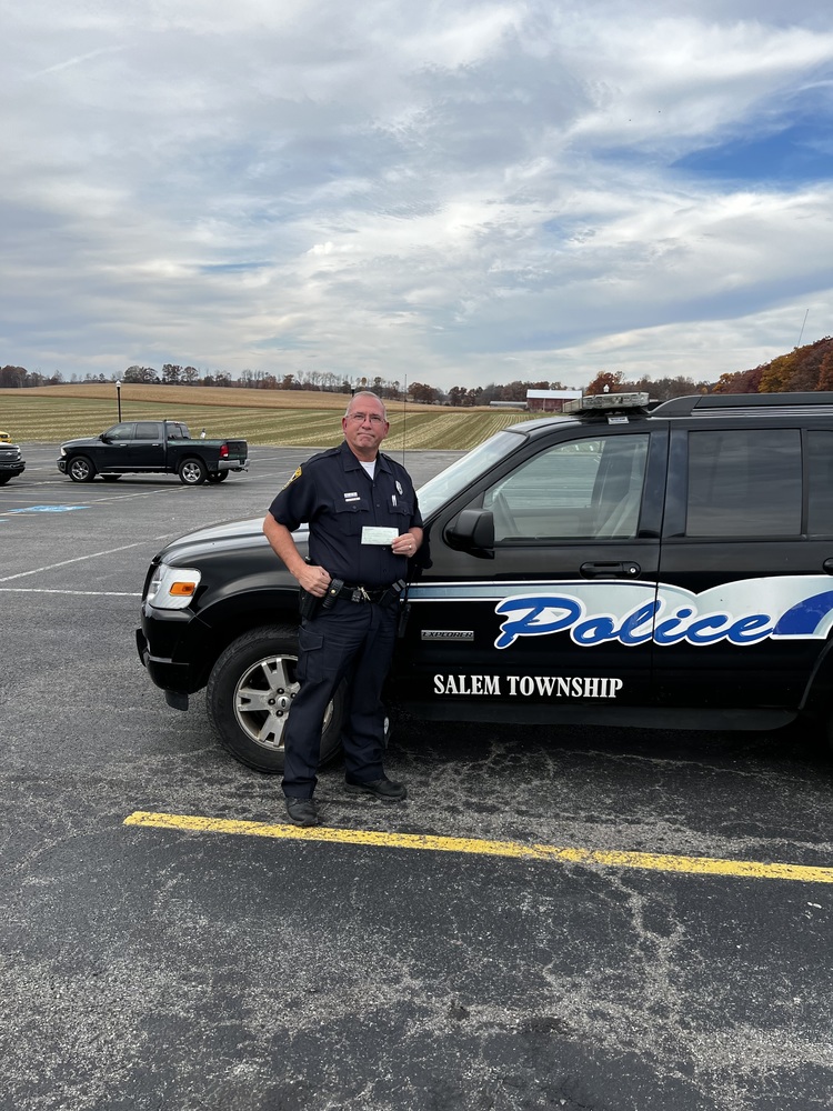 Detective Valentine with check standing in front of police vehicle